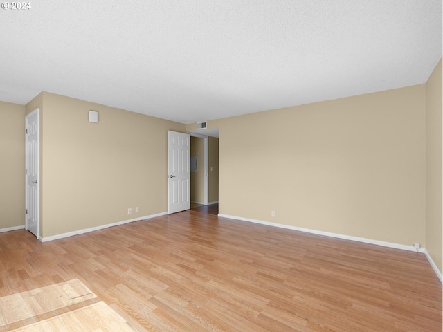 empty room with light wood-style floors, baseboards, visible vents, and a textured ceiling