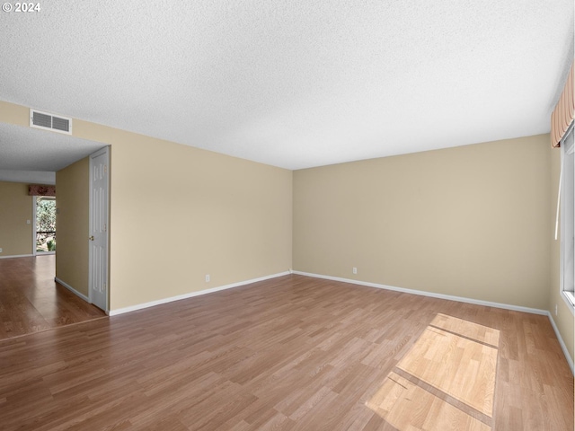 unfurnished room with a textured ceiling, light wood finished floors, visible vents, and baseboards