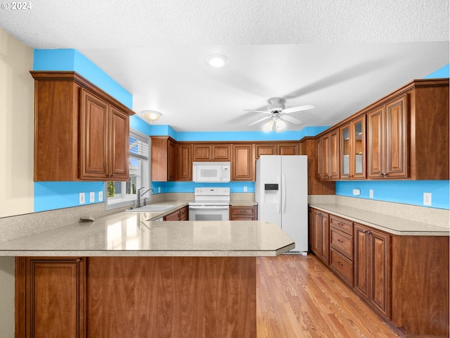 kitchen featuring a peninsula, white appliances, a sink, and brown cabinets