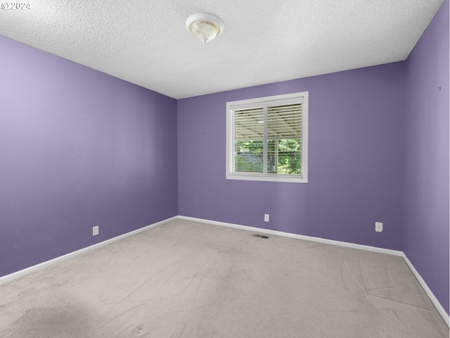 carpeted spare room featuring visible vents, a textured ceiling, and baseboards