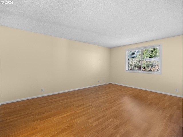 empty room featuring light wood-type flooring, a textured ceiling, and baseboards