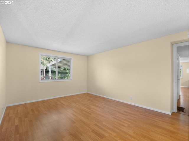 unfurnished room with visible vents, light wood-style flooring, baseboards, and a textured ceiling