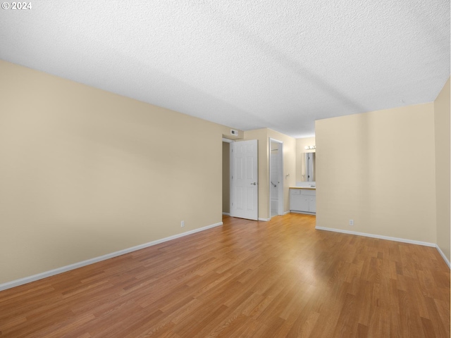 empty room featuring a textured ceiling, light wood finished floors, and baseboards