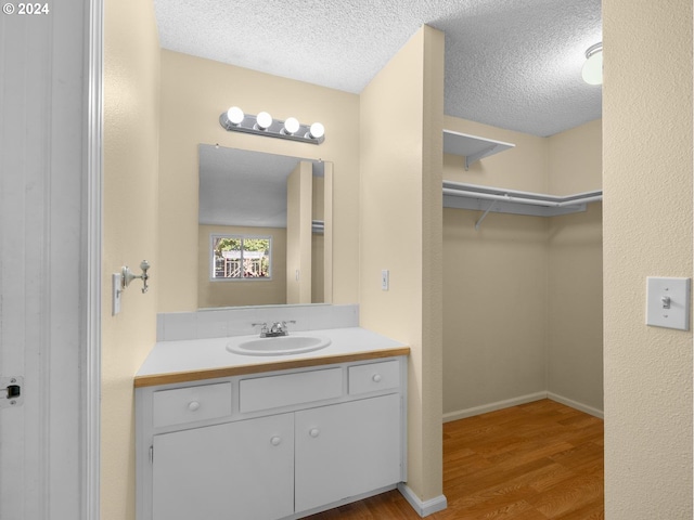 bathroom featuring a spacious closet, a textured ceiling, vanity, wood finished floors, and baseboards