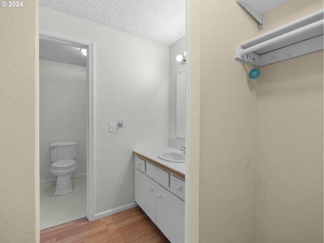 bathroom featuring baseboards, toilet, wood finished floors, a textured ceiling, and vanity