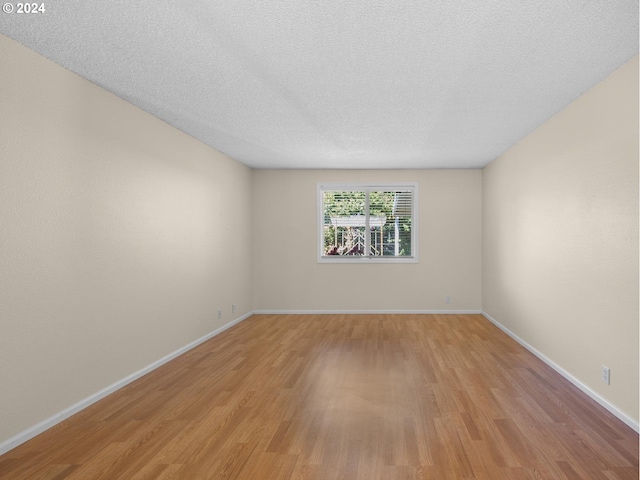 spare room with light wood-style flooring, baseboards, and a textured ceiling