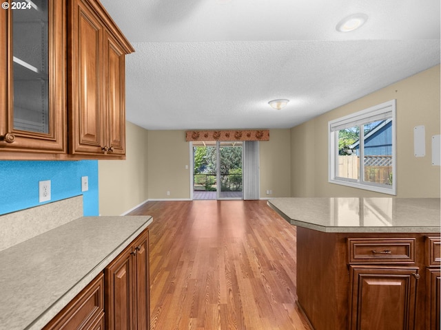 kitchen featuring brown cabinetry, light wood-style flooring, glass insert cabinets, open floor plan, and light countertops