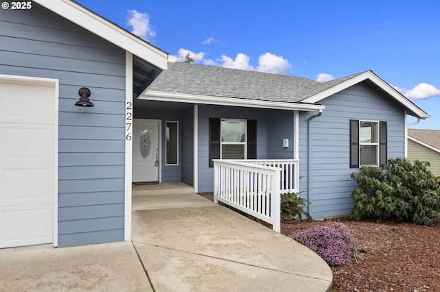 doorway to property featuring an attached garage, a shingled roof, and a porch