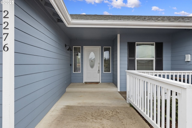 entrance to property featuring a porch and a shingled roof