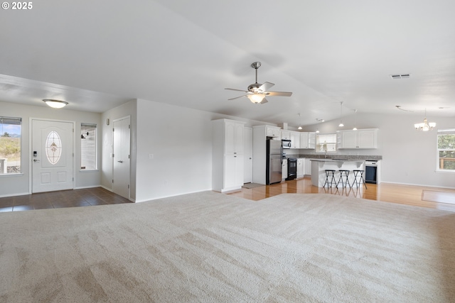 unfurnished living room with light carpet, visible vents, vaulted ceiling, and ceiling fan with notable chandelier