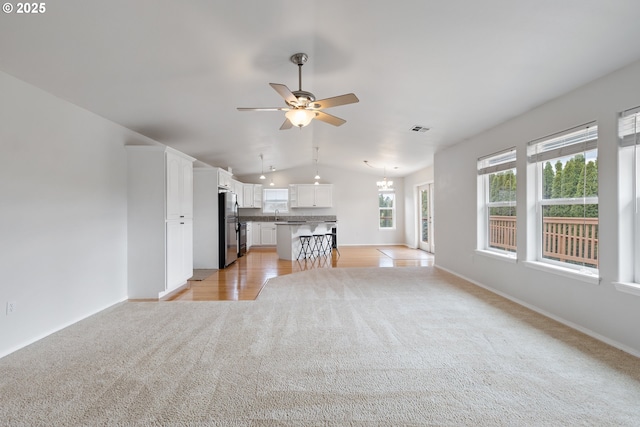 unfurnished living room with light carpet, vaulted ceiling, a sink, baseboards, and ceiling fan with notable chandelier