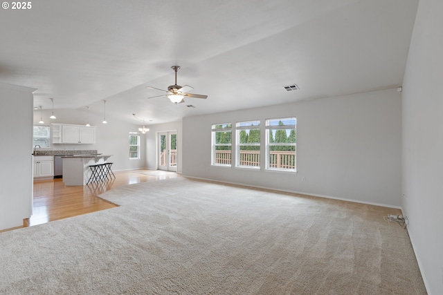 unfurnished living room with a wealth of natural light, vaulted ceiling, a sink, and light colored carpet