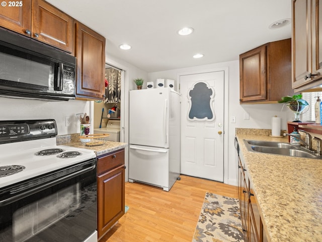 kitchen with light wood finished floors, black microwave, range with electric stovetop, freestanding refrigerator, and a sink