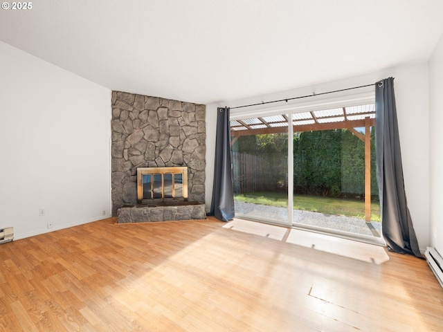 unfurnished living room featuring a baseboard heating unit, a stone fireplace, and wood finished floors