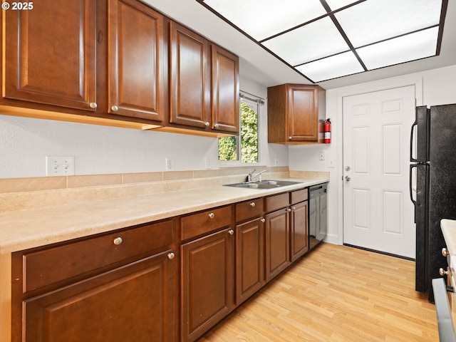 kitchen featuring light countertops, light wood-style floors, brown cabinetry, black appliances, and a sink