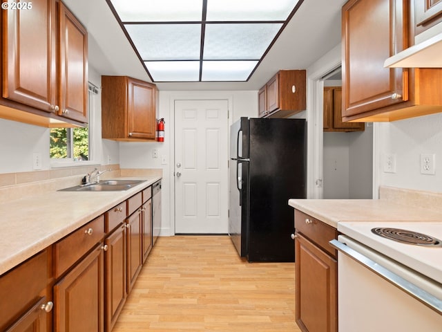 kitchen with a sink, under cabinet range hood, brown cabinets, freestanding refrigerator, and stainless steel dishwasher