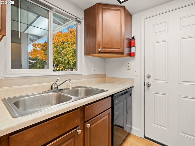 kitchen with brown cabinetry, light wood finished floors, a sink, light countertops, and dishwasher