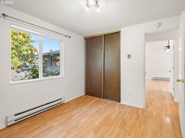 unfurnished bedroom featuring a textured ceiling, a baseboard heating unit, light wood-type flooring, and a baseboard radiator