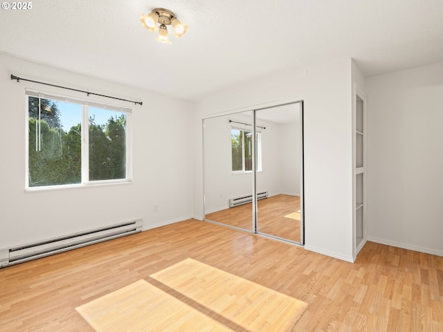 unfurnished bedroom featuring a closet, a baseboard heating unit, baseboards, and wood finished floors