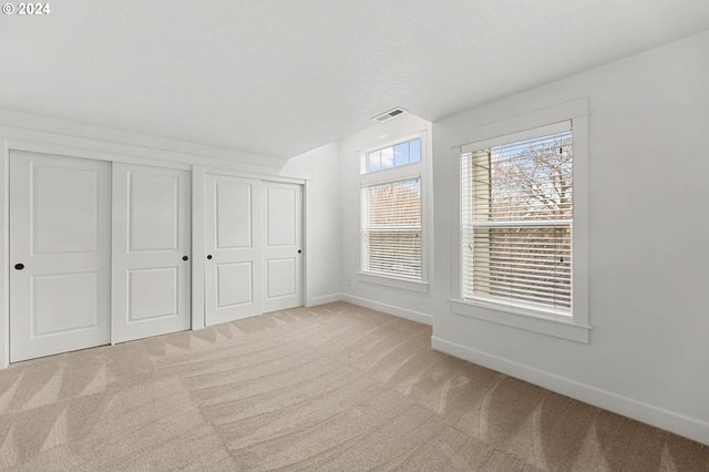 unfurnished bedroom featuring light carpet, baseboards, visible vents, and multiple closets