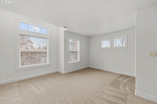 spare room featuring light colored carpet, a textured ceiling, and baseboards