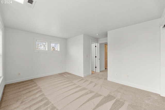 spare room featuring light colored carpet, visible vents, and baseboards