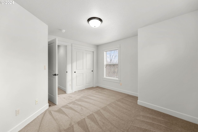 unfurnished bedroom with light carpet, a closet, a textured ceiling, and baseboards