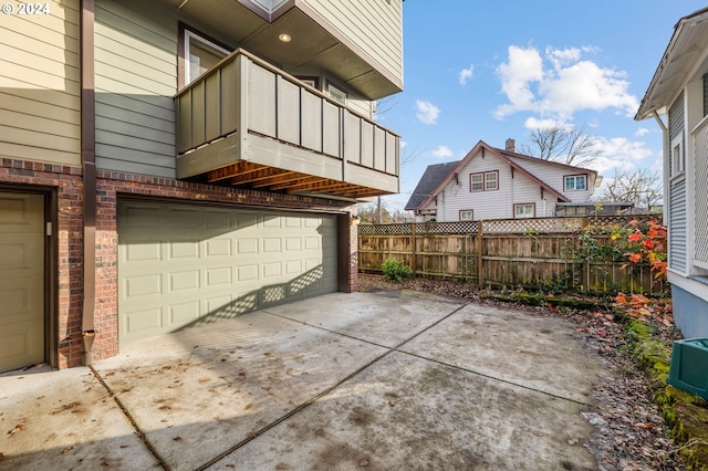 view of patio with an attached garage, a balcony, fence, and concrete driveway