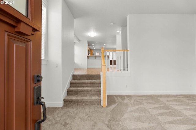 foyer entrance with light colored carpet, stairway, and baseboards