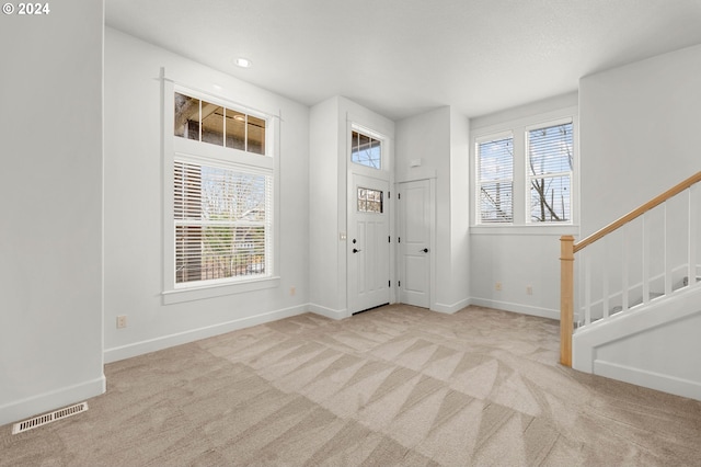 entrance foyer featuring visible vents, stairway, a wealth of natural light, and light colored carpet