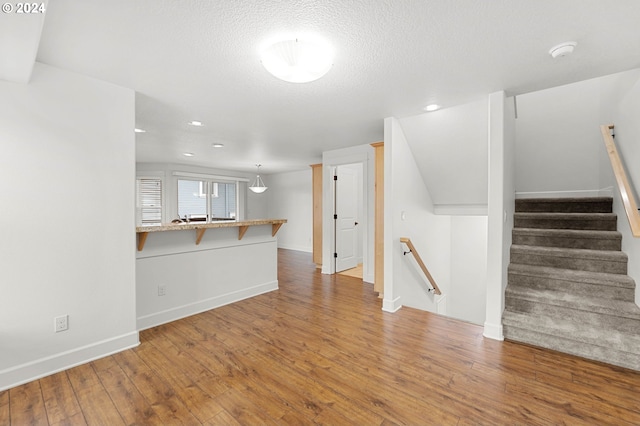 unfurnished living room with a textured ceiling, recessed lighting, wood finished floors, and baseboards