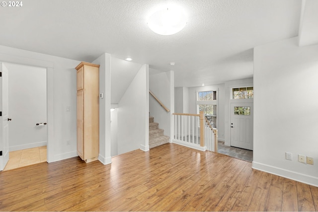 unfurnished room with baseboards, light wood-style flooring, a textured ceiling, and stairs