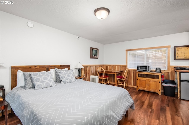 bedroom with a wainscoted wall, radiator heating unit, dark wood finished floors, and a textured ceiling