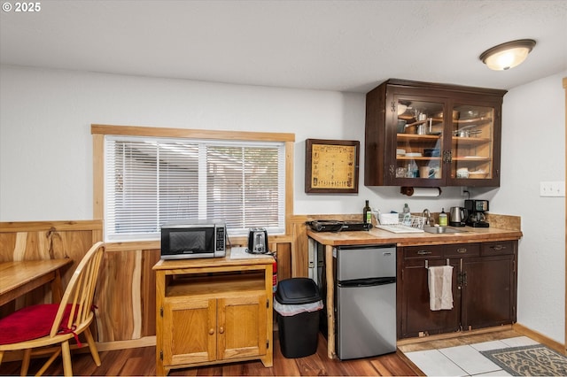 bar featuring light wood finished floors, wainscoting, stainless steel microwave, refrigerator, and a sink