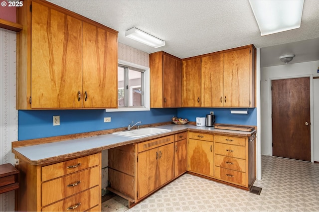 kitchen featuring a textured ceiling, light floors, a sink, and brown cabinets