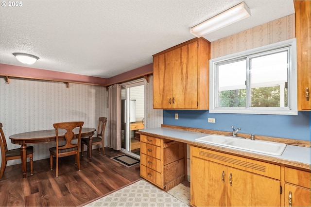 kitchen featuring light countertops, a sink, a textured ceiling, wood finished floors, and wallpapered walls