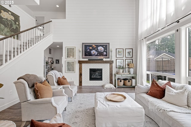 living room featuring a tiled fireplace, wood-type flooring, and a towering ceiling