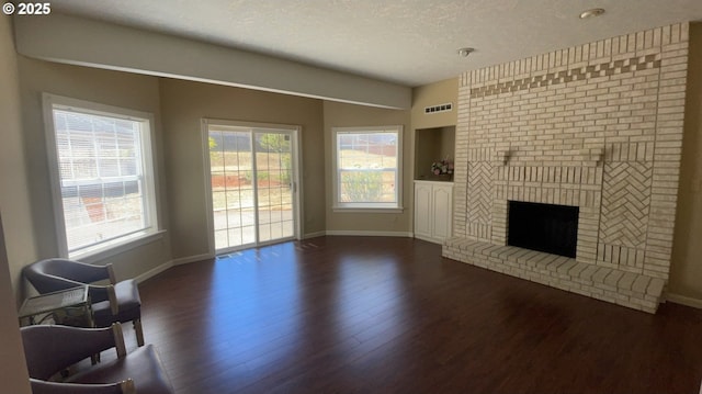 living room with a brick fireplace, dark wood-type flooring, and a textured ceiling