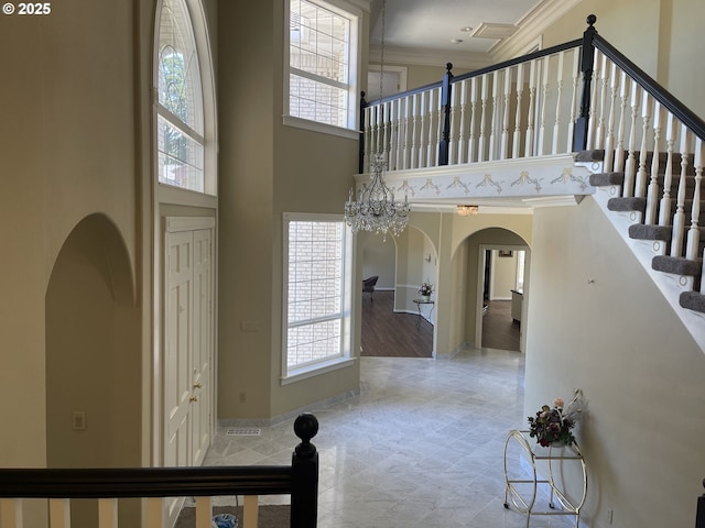 foyer entrance featuring crown molding, a chandelier, a healthy amount of sunlight, and a towering ceiling