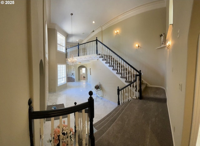 stairway featuring crown molding, carpet, a towering ceiling, and a notable chandelier