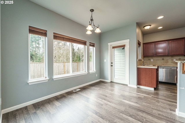 unfurnished dining area featuring visible vents, a sink, wood finished floors, an inviting chandelier, and baseboards