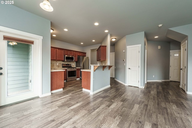 kitchen with dark wood finished floors, appliances with stainless steel finishes, a kitchen bar, and a peninsula