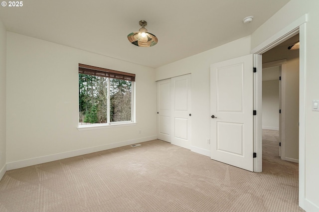 unfurnished bedroom featuring visible vents, light colored carpet, baseboards, and a closet