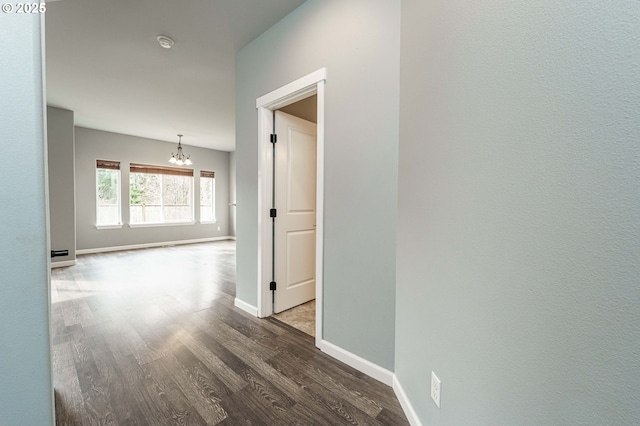 hallway featuring wood finished floors, baseboards, and a chandelier