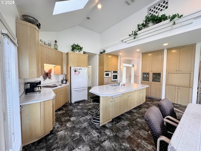 kitchen featuring a kitchen island, a skylight, a breakfast bar area, light brown cabinets, and white appliances