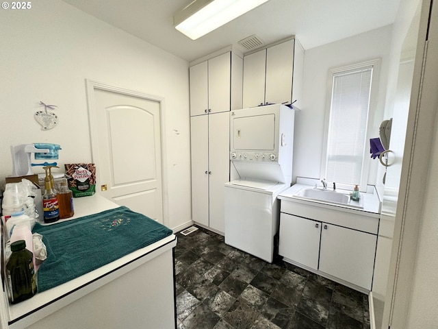 laundry room featuring cabinets, stacked washer and clothes dryer, and sink