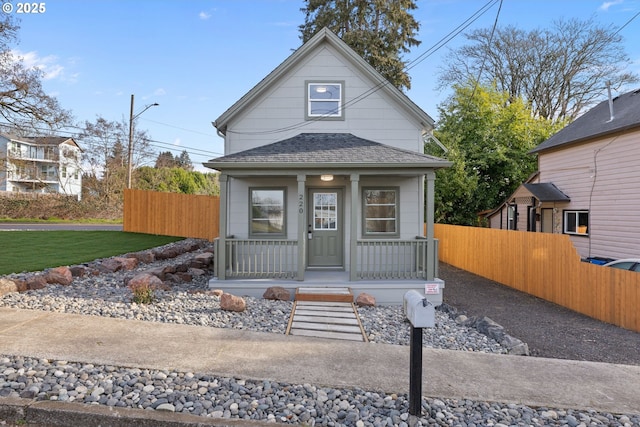 view of front of property with covered porch, a shingled roof, and fence