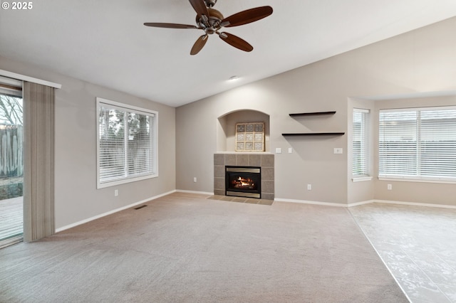 unfurnished living room featuring lofted ceiling, a tiled fireplace, light carpet, and ceiling fan