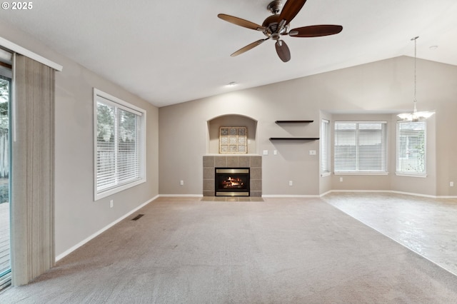 unfurnished living room featuring a tiled fireplace, a wealth of natural light, vaulted ceiling, and light carpet