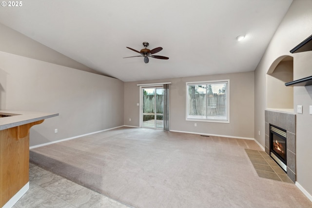 unfurnished living room with ceiling fan, light colored carpet, lofted ceiling, and a tiled fireplace